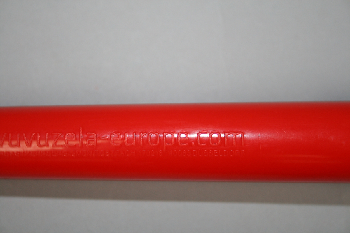 Trompett i tre deler av hvit og rødt plast, tilsvarende farger til Sveits landslag i fotball. Grunntone "B". Demontert kan delene oppbevares inn i hverandre for transport.
