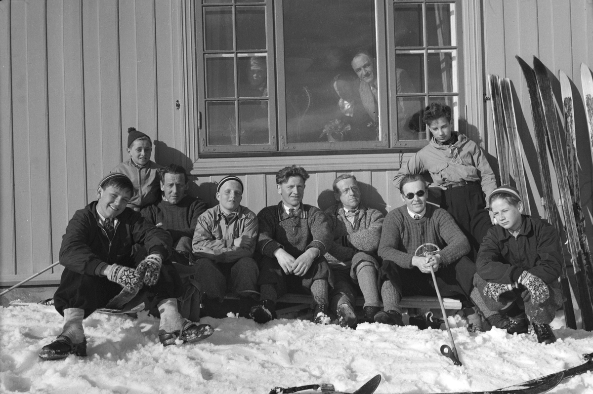 Ukjent gruppe mennesker soler seg i husveggen på skitur. Ski. 