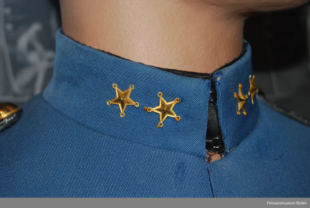 Mellanblå med krage i samma färg försedd med två stjärnor betecknande löjtnant. Framtill dold knäppning med 7 knappar i enkel rad. Axeltränsar m/1871 av dubbla silverfärgade fyrkantsgaloner med knappar av regementets modell.