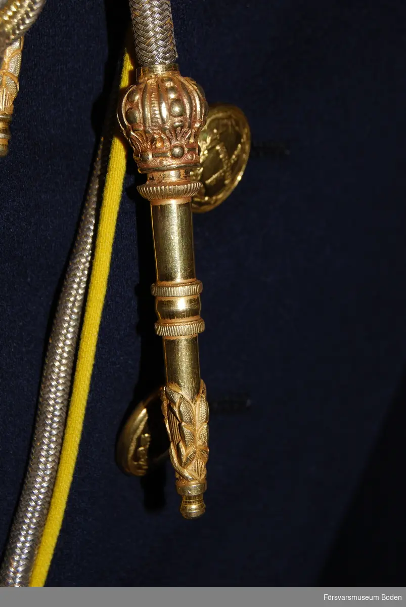 Flätade snören i guld med spetsformade avslutningsstycken med dekor.