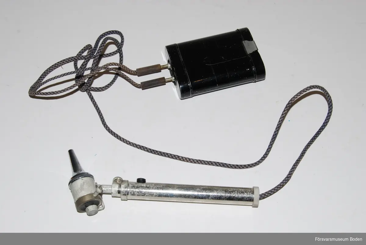 Otoskop med batteribox, men övriga tillbehör saknas. Används för öronundersökningar. Utbytbara munstycken med bajonettfattning. Vridbar försättslins vid okularet samt munstycke för luftslang. Handtaget har en strömbrytare för belysningen. Batteriboxen är avsedd för 4,5 V ficklamsbatteri.Tillverkat i Tyskland och märkt 1934, vilket eventuellt kan vara tillverkningsår. Också märkt D.R.M.G., vilket är en form av mönsterskydd och står för Deutsches Reichsgebrauchsmuster. Förkortningen användes på tyska produkter t.o.m. 1952.