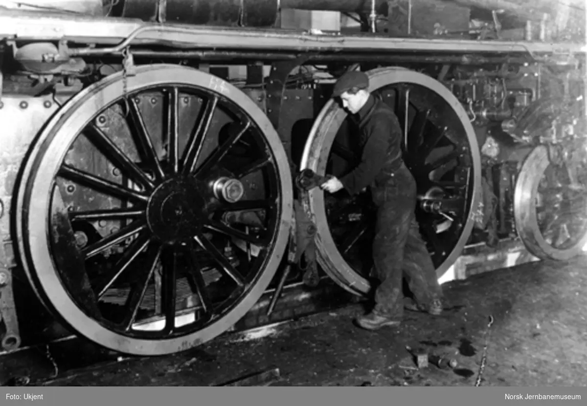 En verkstedarbeider monterer bremseklosser ved hovedrevisjon av damplokomotiv, trolig på Thunes mekaniske værksted