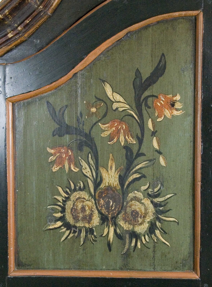 Skap i over- og underdel. Ovedelen har skjehylle og plass til skuffer. Buet topplist satt sammen av vinkelskårete deler. Blomstermalt.