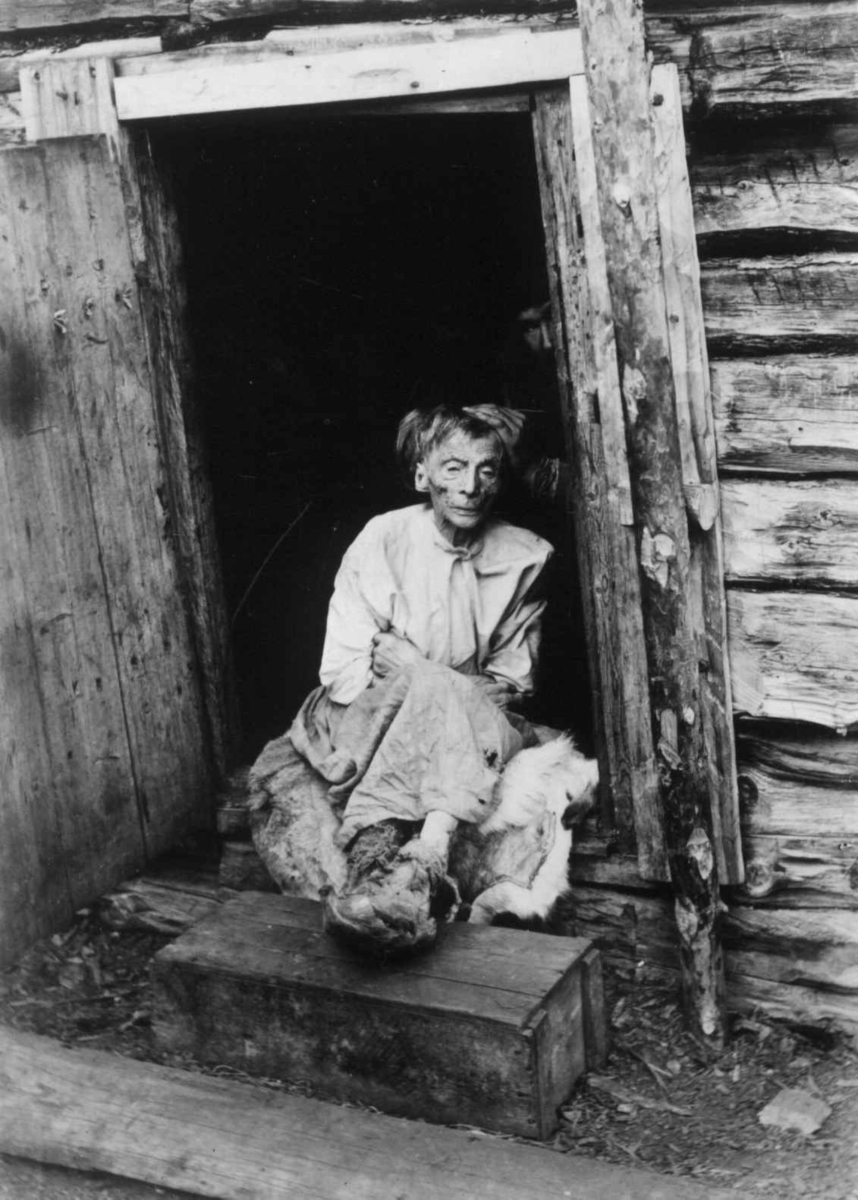 Portrett av Kristine Ærillæ (finsk, Ärilä), Laitimor, støttet opp i døråpning for fotografering i september 1898. Hun er her i sitt 96. år og fra Vaggatem i Sør-Varanger i Finnmark.