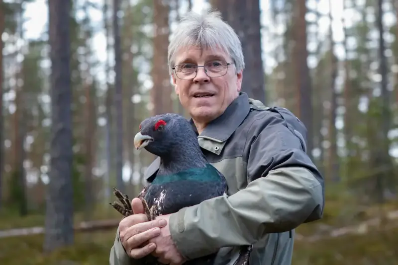 Portrett av Trond Berg. Han har på seg grønn jakke og briller. I hendene holder han en tiur. 